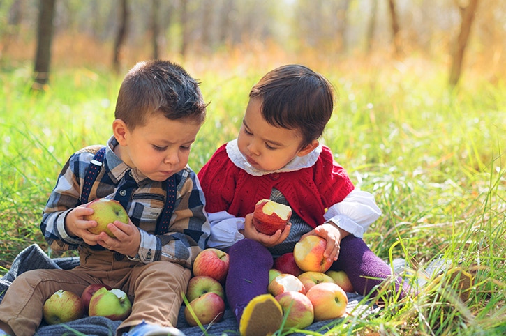 par de niños comiendo manzanas sobre el pasto aprovechando los beneficios de la fructuosa