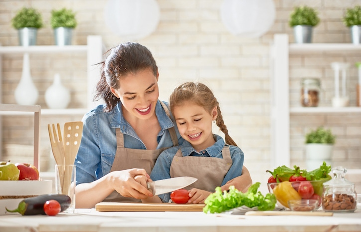Mandre e hija en la cocina cortando con un cuchillo un jitomate aprendiendo sobre nutrición para niños